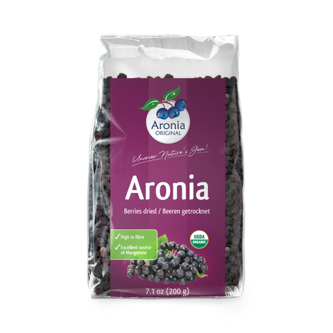 Dried aronia berries next to a glass of aronia juice
