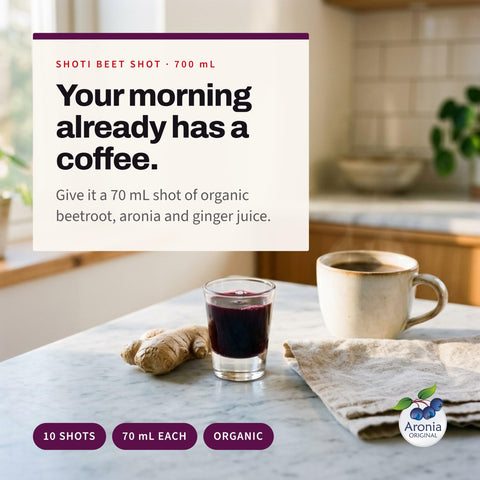 Serving suggestion: Small glass of Shoti Beet Shot next to a coffee cup and ginger root on a kitchen counter