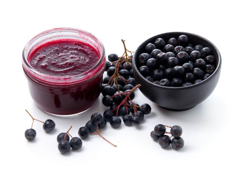 Fresh aronia berries next to a jar of aronia jam