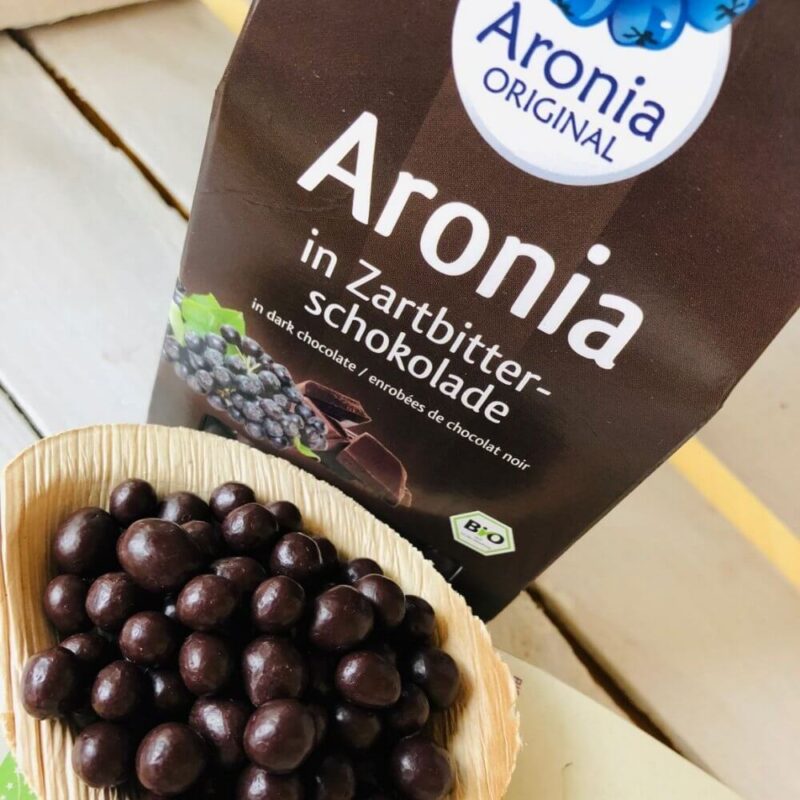 dried aronia berries covered with dark chocolate on wooden spoon